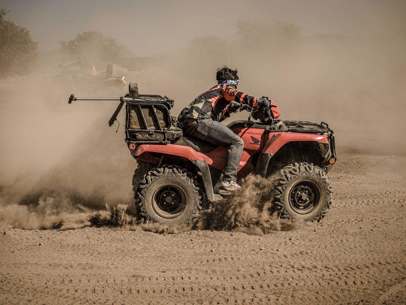 A rider powering a quad bike through dust on an off road sand trail