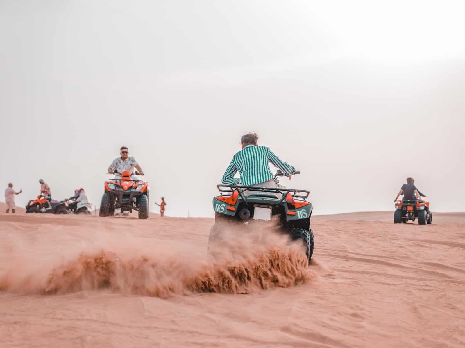 A group of riders on quad bikes crossing open sand dunes on a bright day