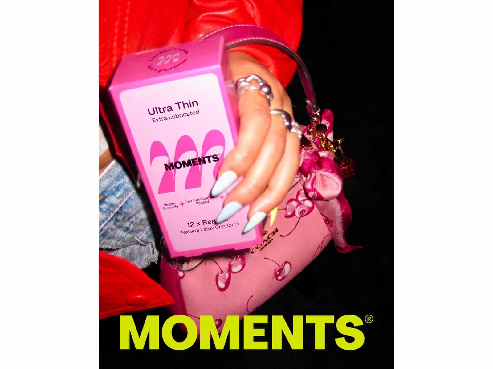 A hand with pink nails holding a box of Moments Ultra Thin condoms against a black background
