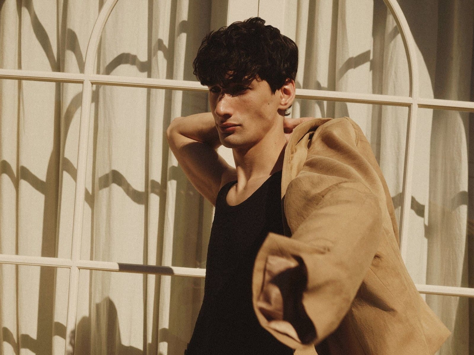 A man in a black singlet with the dune linen Host Tux slung over his shoulder in front of arched windows.
