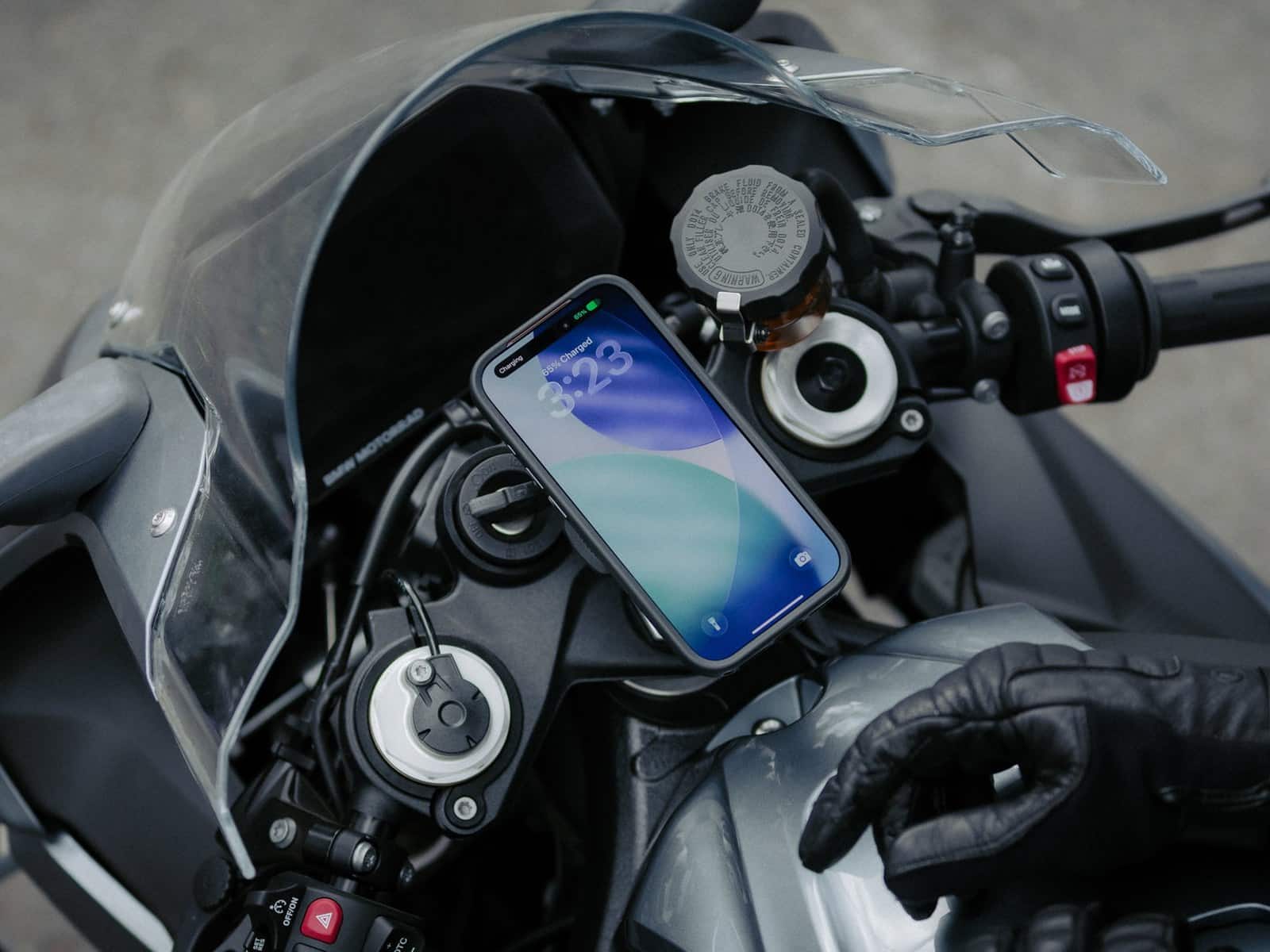 A phone in a Quad Lock case locked to a motorcycle handlebar mount with a gloved hand resting on the grip