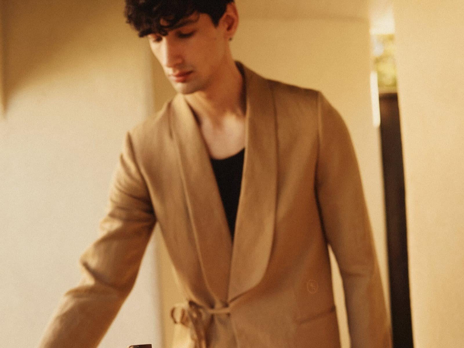 A man wearing the dune linen Host Tux with a shawl lapel and tie closure, standing behind a bottle of Woodford Reserve on a table.