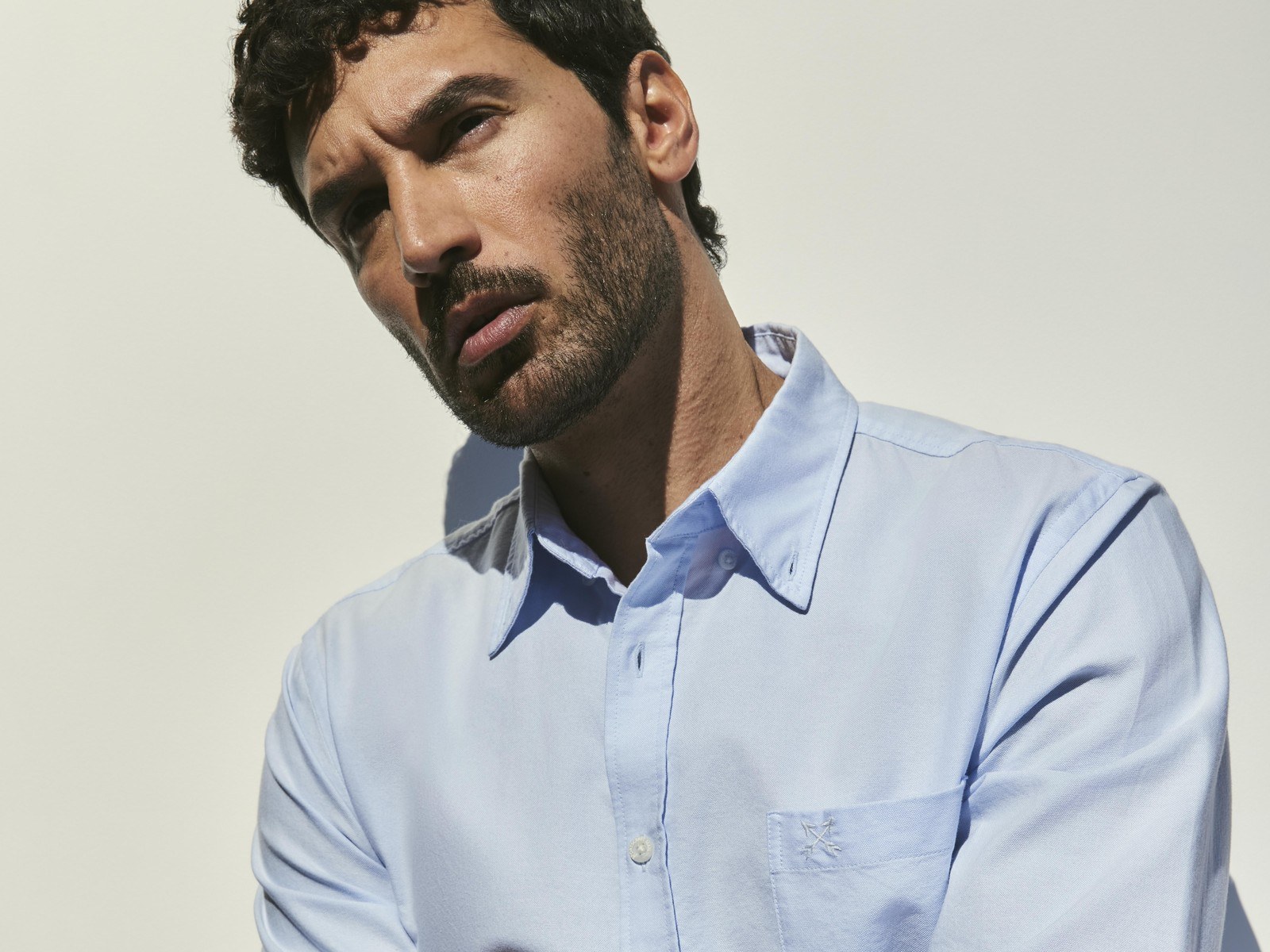 A man wearing the Sportscraft Long Sleeve Oxford Shirt in Light Blue with his arms crossed against a white wall