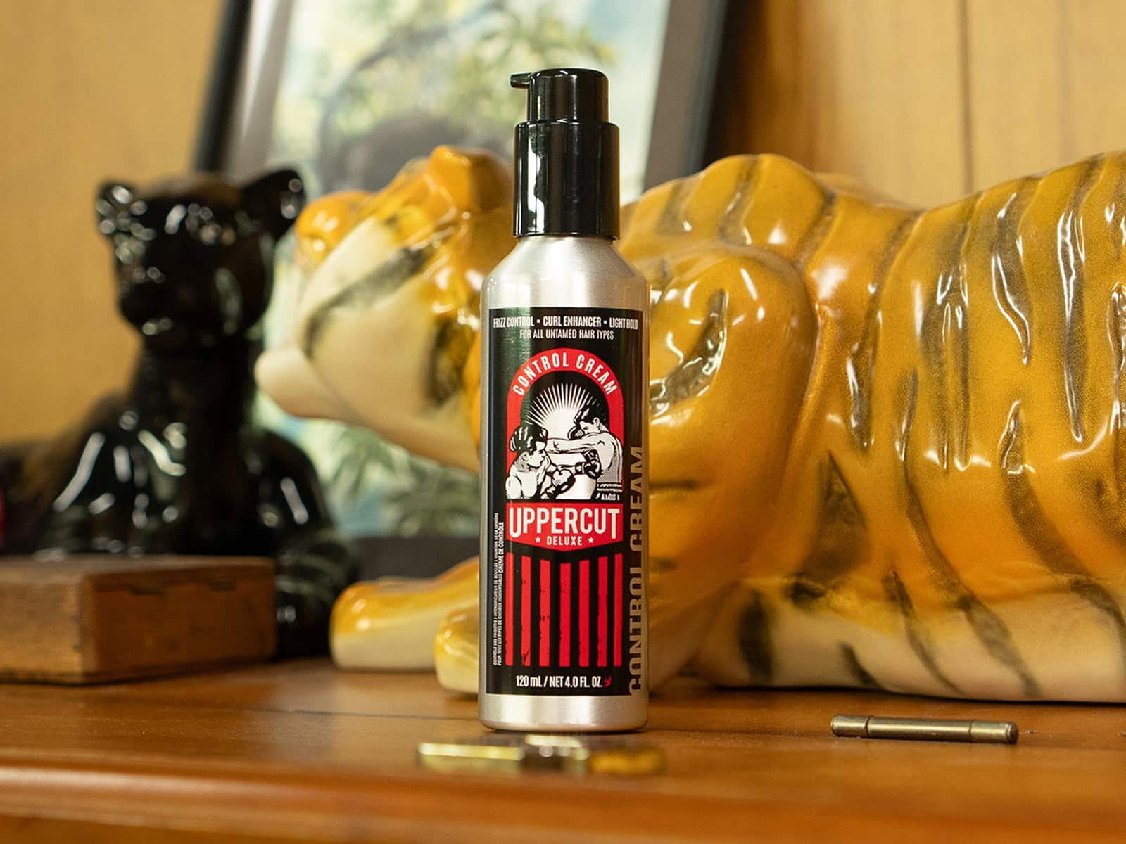 Uppercut Deluxe Control Cream standing on a timber dresser in front of a ceramic tiger ornament and a black panther figurine.