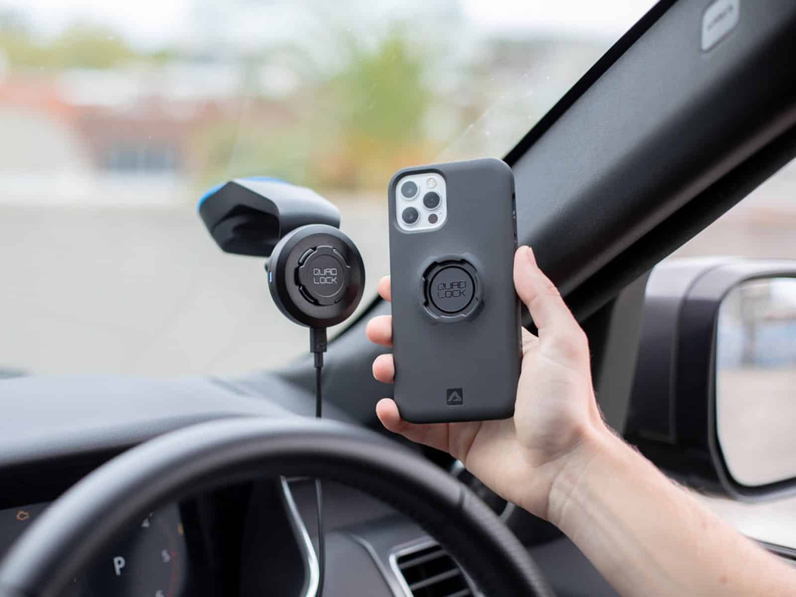 A hand holding a phone in a Quad Lock case beside a Quad Lock car mount fitted inside a car