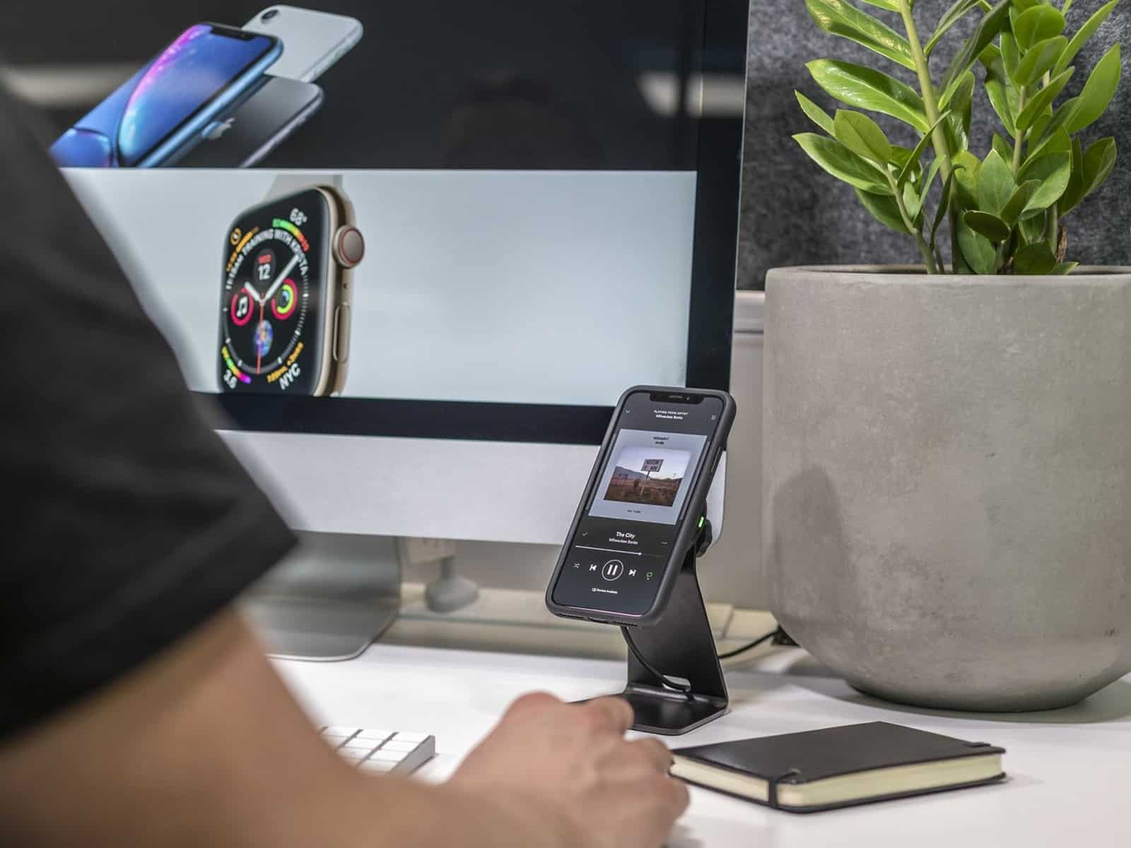 A Quad Lock desk mount holding a phone upright on a desk beside a monitor