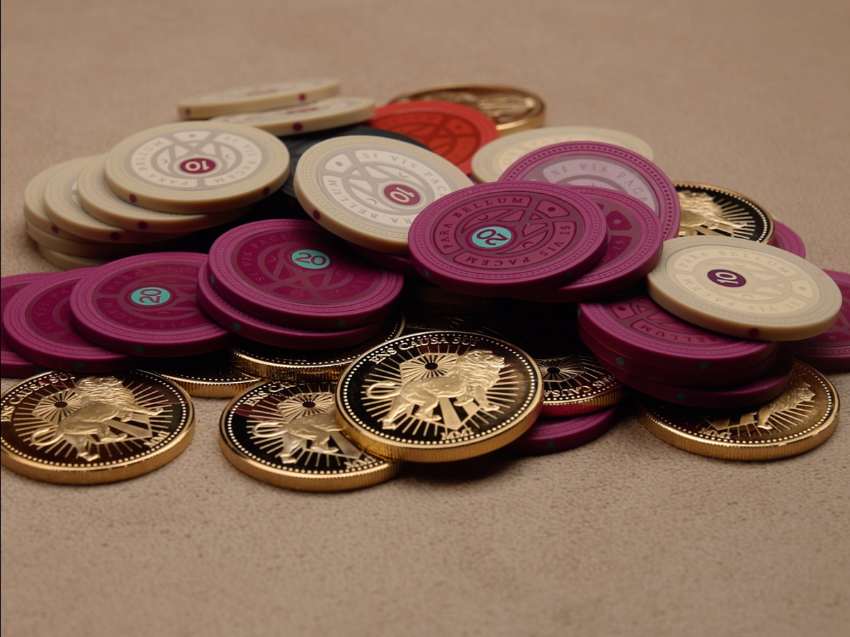 Clay chips from the Official John Wick Poker Set in burgundy and cream with Continental gold coins piled on a felt table