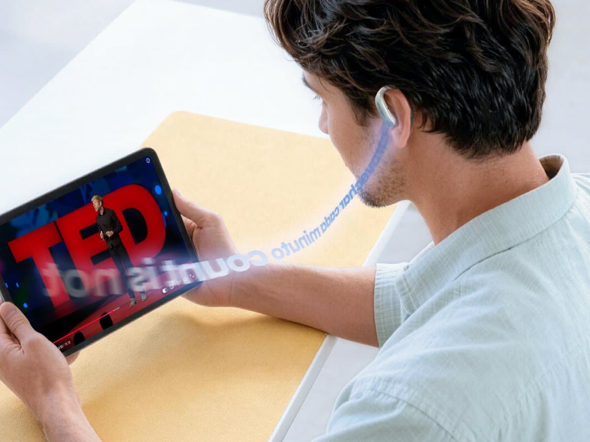 A man wearing a Timekettle LiveTalk earbud watches a talk on a tablet with translated subtitles