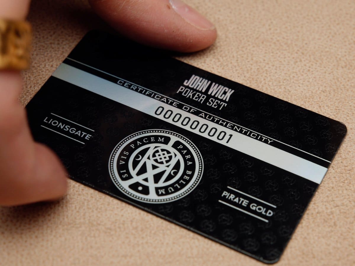 A black serialised certificate of authenticity card for the John Wick Poker Set held on a tan surface