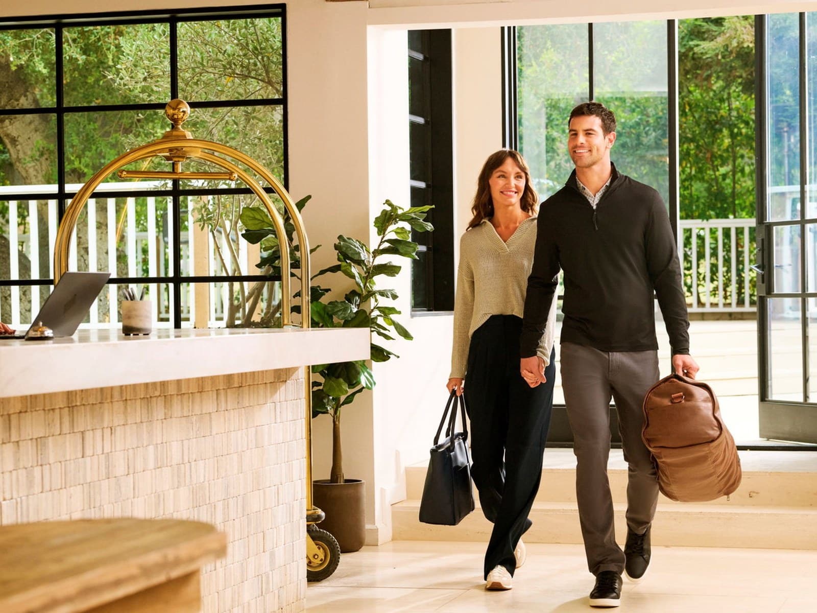 A couple walking through a hotel lobby, the man in a black quarter-zip sweater and grey trousers