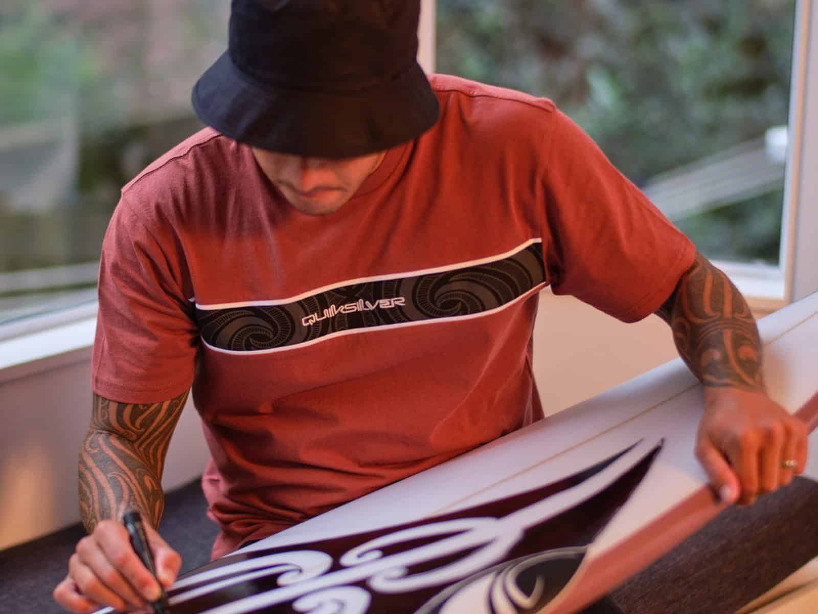 Kehu Butler drawing Tai Kehu artwork onto a surfboard blank
