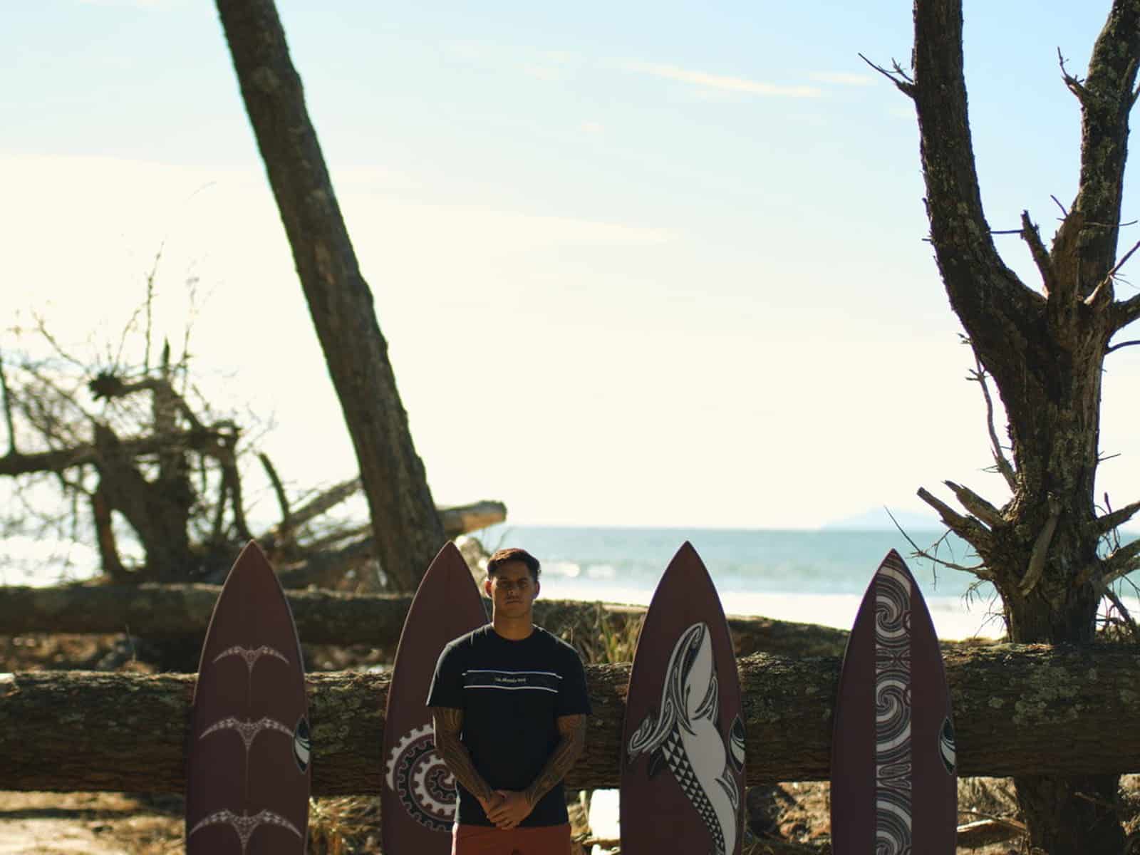 Kehu Butler standing among the custom SharpEye Tai Kehu surfboards on a beach