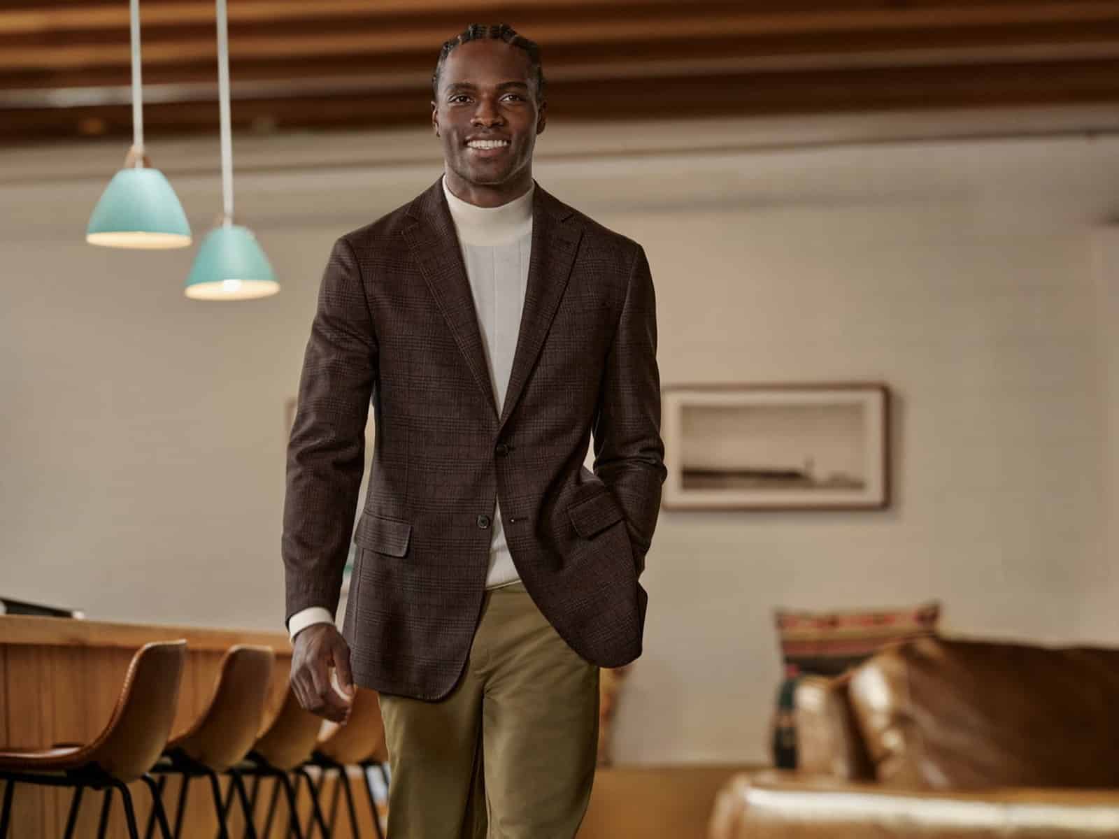 A man in a brown check sport coat, white turtleneck and chinos in a modern office